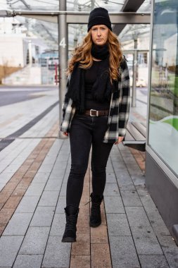 Otuzlu yaşlarda, uzun kızıl saçlı, kep takan ve şehir merkezinde siyah giyinen bir kadın..