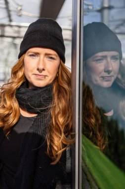 Otuzlu yaşlarda, uzun kızıl saçlı, kep takan ve şehir merkezinde siyah giyinen bir kadın..