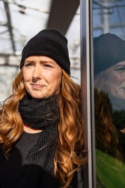 Otuzlu yaşlarda, uzun kızıl saçlı, kep takan ve şehir merkezinde siyah giyinen bir kadın..