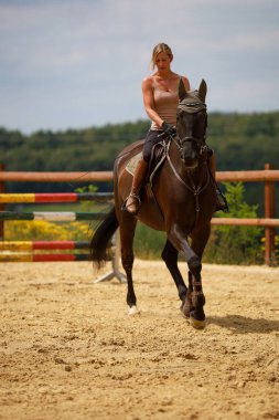 Atın üstünde kolsuz bluz giyen genç bir kadın dörtnala, portre biçiminde bir dönüş yapıyor..