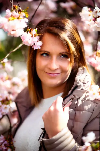 One young woman stands in a sea of cherry blossoms and smiles into the camera. Cherry blossoms on the tree in full pink bloom.
