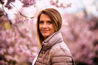 Genç bir kadın kiraz çiçekleri denizinde duruyor ve kameraya gülümsüyor. Ağaçtaki kiraz çiçekleri tamamen pembe açarlar..