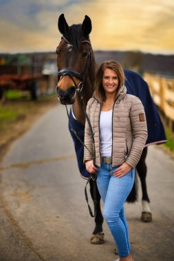 Arka planda dramatik bir gökyüzü olan bir yolda at taşıyan kadın..