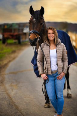 Arka planda dramatik bir gökyüzü olan bir yolda at taşıyan kadın..