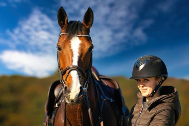 Mavi gökyüzüne karşı bir at kafasının portresi, binici atın yanında duruyor. Doğada güneşli bir sonbahar günü.