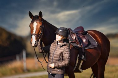 Sonbahar doğasında, gün ışığında yanında binicisi olan bir çayırdaki at..