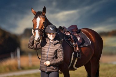 Sonbahar doğasında, gün ışığında yanında binicisi olan bir çayırdaki at..