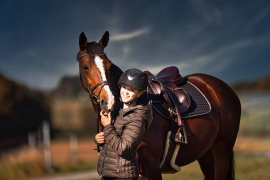 Sonbahar doğasında, gün ışığında yanında binicisi olan bir çayırdaki at..