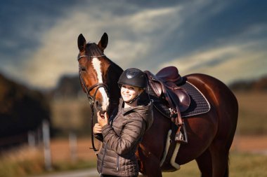 Sonbahar doğasında, gün ışığında yanında binicisi olan bir çayırdaki at..