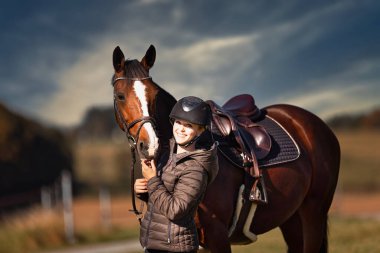 Sonbahar doğasında, gün ışığında yanında binicisi olan bir çayırdaki at..