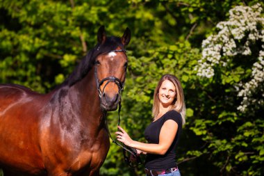 Siyah gömlekli, kısa çizgili esmer saçlı, gün ışığında atının yanında portresi olan genç bir kadın. Kadında keskinlik seviyesi var. Görüntü biçimi bulanık arkaplan ile renklidir.