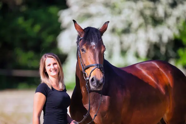 Genç bir kadın sıcak bir bahar gününün güneşinde atıyla portrede dikiliyor ve arka planda çiçek açan bir dikenli çalı var. Metin için boşluk olan manzara biçiminde resim.