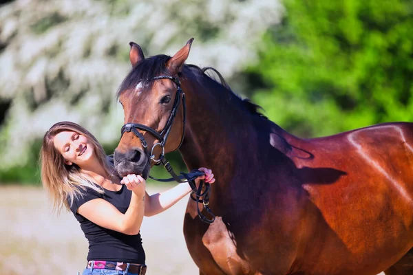 Genç bir kadın sıcak bir bahar gününün güneşinde atıyla portrede dikiliyor ve arka planda çiçek açan bir dikenli çalı var. Metin için boşluk olan manzara biçiminde resim.