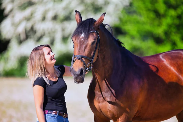 Genç bir kadın sıcak bir bahar gününün güneşinde atıyla portrede dikiliyor ve arka planda çiçek açan bir dikenli çalı var. Metin için boşluk olan manzara biçiminde resim.