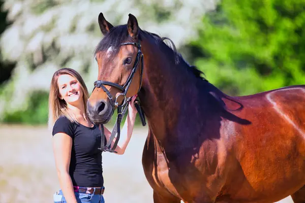 Genç bir kadın sıcak bir bahar gününün güneşinde atıyla portrede dikiliyor ve arka planda çiçek açan bir dikenli çalı var. Metin için boşluk olan manzara biçiminde resim.