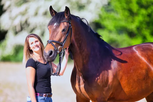 Genç bir kadın sıcak bir bahar gününün güneşinde atıyla portrede dikiliyor ve arka planda çiçek açan bir dikenli çalı var. Metin için boşluk olan manzara biçiminde resim.