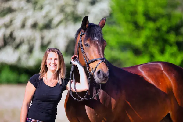 Genç bir kadın sıcak bir bahar gününün güneşinde atıyla portrede dikiliyor ve arka planda çiçek açan bir dikenli çalı var. Metin için boşluk olan manzara biçiminde resim.