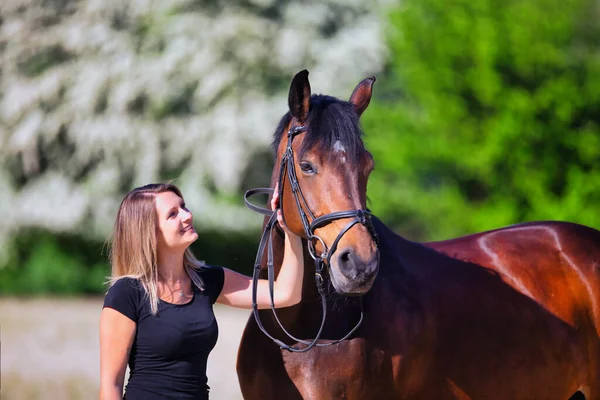 Genç bir kadın sıcak bir bahar gününün güneşinde atıyla portrede dikiliyor ve arka planda çiçek açan bir dikenli çalı var. Metin için boşluk olan manzara biçiminde resim.