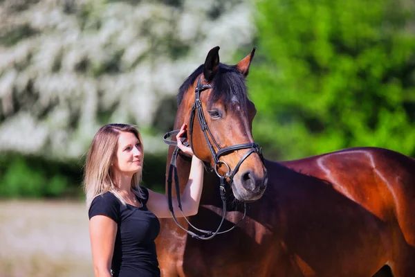 Genç bir kadın sıcak bir bahar gününün güneşinde atıyla portrede dikiliyor ve arka planda çiçek açan bir dikenli çalı var. Metin için boşluk olan manzara biçiminde resim.