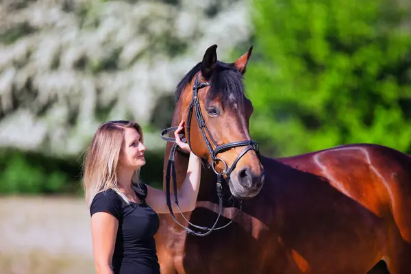 Genç bir kadın sıcak bir bahar gününün güneşinde atıyla portrede dikiliyor ve arka planda çiçek açan bir dikenli çalı var. Metin için boşluk olan manzara biçiminde resim.