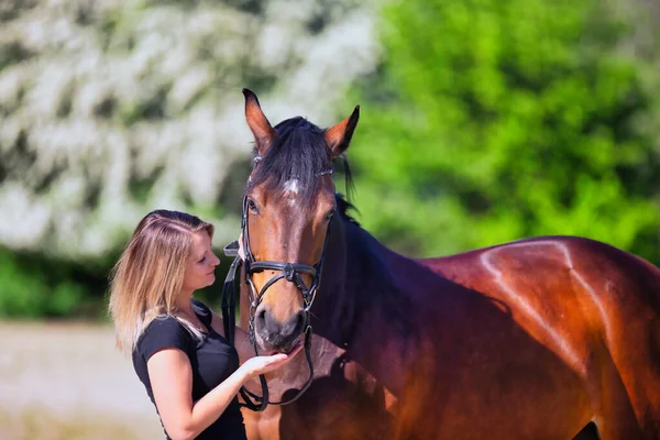 Genç bir kadın sıcak bir bahar gününün güneşinde atıyla portrede dikiliyor ve arka planda çiçek açan bir dikenli çalı var. Metin için boşluk olan manzara biçiminde resim.