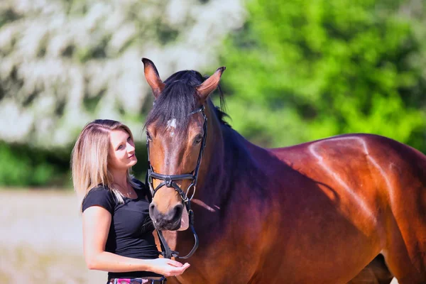 Genç bir kadın sıcak bir bahar gününün güneşinde atıyla portrede dikiliyor ve arka planda çiçek açan bir dikenli çalı var. Metin için boşluk olan manzara biçiminde resim.