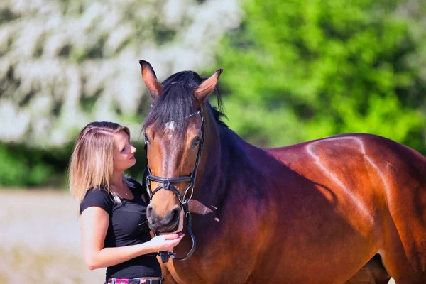 Genç bir kadın sıcak bir bahar gününün güneşinde atıyla portrede dikiliyor ve arka planda çiçek açan bir dikenli çalı var. Metin için boşluk olan manzara biçiminde resim.