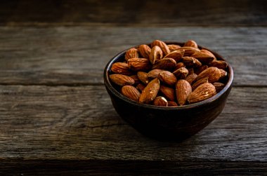 Almond nuts in earthenware on a wooden background.