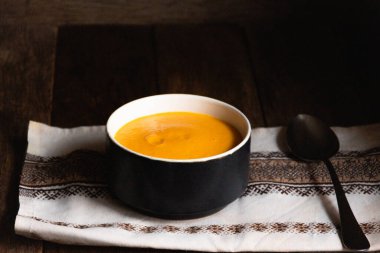 Pumpkin puree soup in a ceramic bowl on a wooden table with a folklore kitchen napkin.