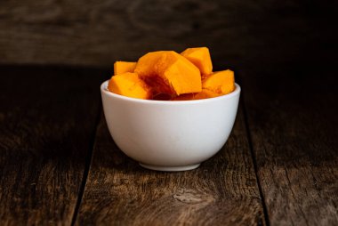 Sliced pumpkin in a white bowl on a wooden table.