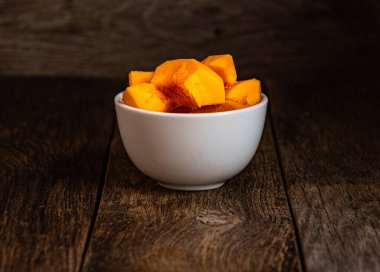 Sliced pumpkin in a white bowl on a wooden table.