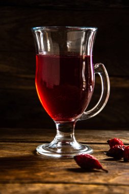 Rosehip tea in a glass cup on a wooden background.