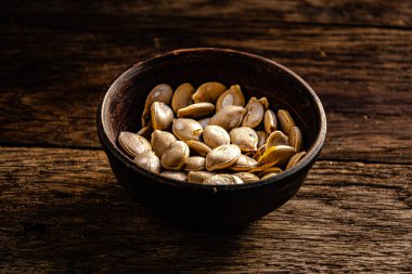 Pumpkin seeds in a ceramic dish on wooden boards.
