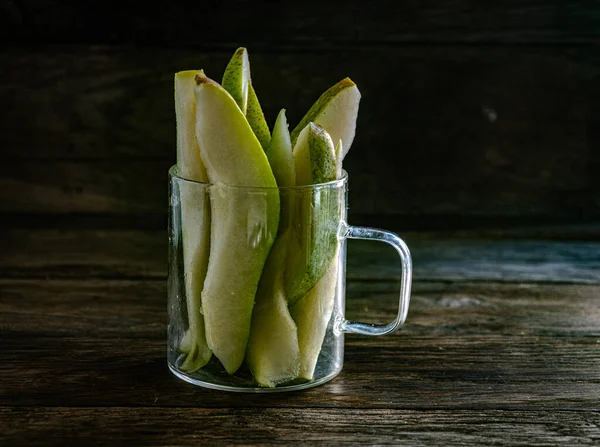 Sliced pear in a glass cup on a kitchen wooden table.