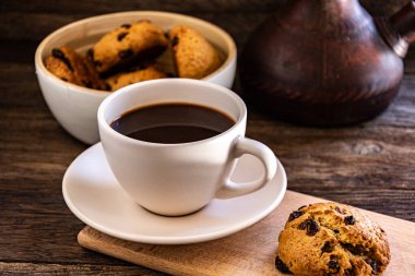 A cup of coffee and oatmeal cookies on the kitchen table.