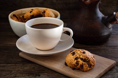 A cup of coffee and oatmeal cookies on the kitchen table.