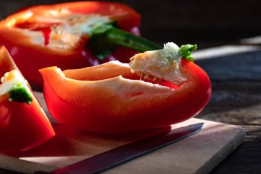 Red bell pepper lies sliced on a cutting board and a knife on the kitchen table. Cooking at home.