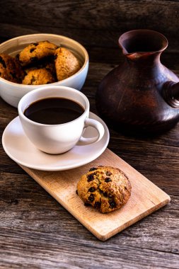 A cup of coffee and oatmeal cookies on the kitchen table.