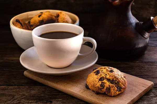 A cup of coffee and oatmeal cookies on the kitchen table.