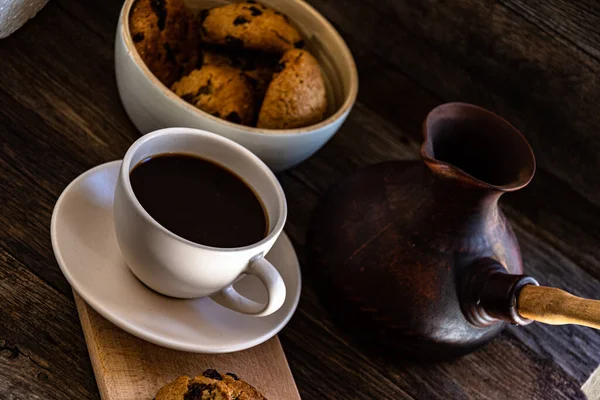 A cup of coffee and oatmeal cookies on the kitchen table.