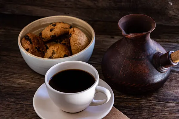 A cup of coffee and oatmeal cookies on the kitchen table.