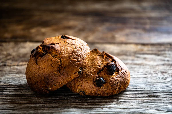Two oatmeal raisin cookies lie on a wooden table.