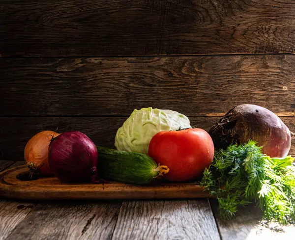 Onions, cabbage, tomatoes, cucumbers, beets, parsley, and herbs lie on a cutting board in the kitchen, on a wooden table.