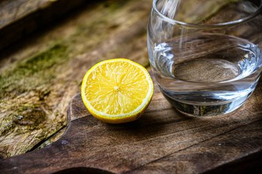 Bir bardak su ve içinde meyve, limon ve kireç olan seramik bir tabak kırsal bir mutfakta ahşap bir masada..