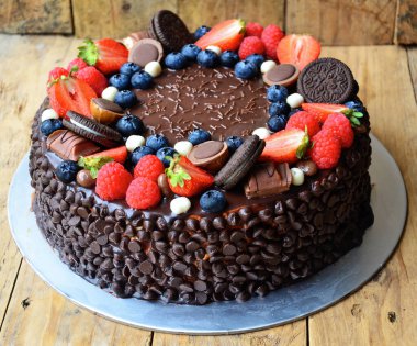 Üstünde çilek, yaban mersini ve yulaflı kurabiye olan çikolatalı pasta. Pasta çikolata parçacıklarıyla süslenmiş ve ev yapımı bir havası var.