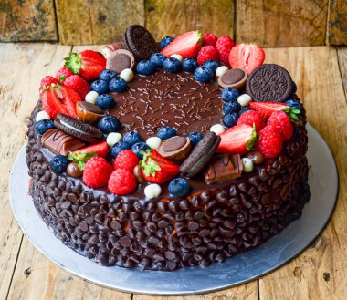 Üstünde çilek, yaban mersini ve yulaflı kurabiye olan çikolatalı pasta. Pasta çikolata parçacıklarıyla süslenmiş ve ev yapımı bir havası var.