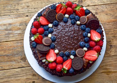 Üstünde çilek, yaban mersini ve yulaflı kurabiye olan çikolatalı pasta. Pasta çikolata parçacıklarıyla süslenmiş ve ev yapımı bir havası var.