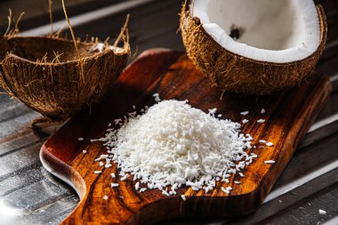 Kırık bir hindistan cevizi ahşap bir mutfak tahtasının üzerinde duruyor taze eti ışıkta parlıyor ve hindistan cevizi kupası sanki sizi tropikal havanın tadını çıkarmaya davet ediyormuş gibi duruyor. Bu çekim yaz atmosferini, hafifliği ve doğal güzelliği yansıtıyor.. 