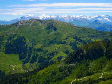 Bir yaz günü Saalbach Hinterglemm kayak merkezi yakınlarındaki dağlara, yeşil çayırlara, dağlara, mavi gökyüzüne, bulutlara, arka planda buzullarla Hohen Tauern dağlarına bakın. Alpler, Avusturya. 