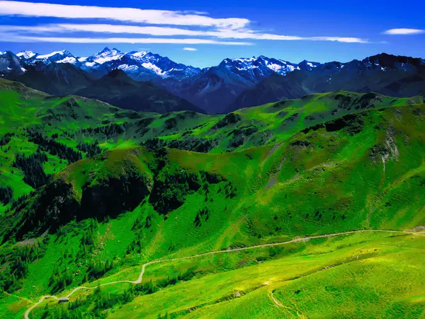 Bir yaz günü Saalbach Hinterglemm kayak merkezi yakınlarındaki dağlara, yeşil çayırlara, dağlara, mavi gökyüzüne, bulutlara, arka planda buzullarla Hohen Tauern dağlarına bakın. Alpler, Avusturya. 